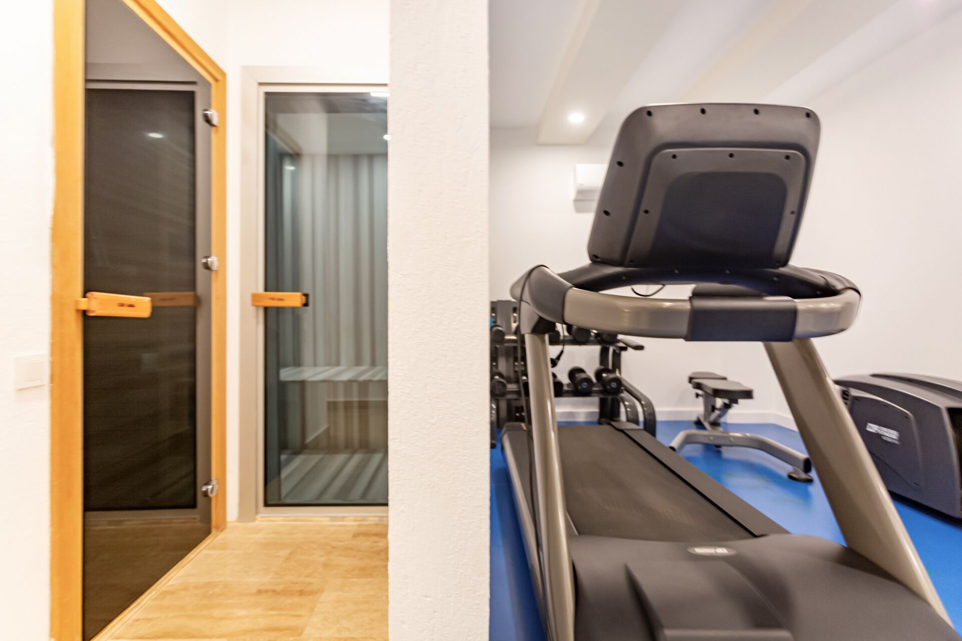 A room with a treadmill, a door leading to a balcony, and a window with curtains.