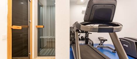 A room with a treadmill, a door leading to a balcony, and a window with curtains.
