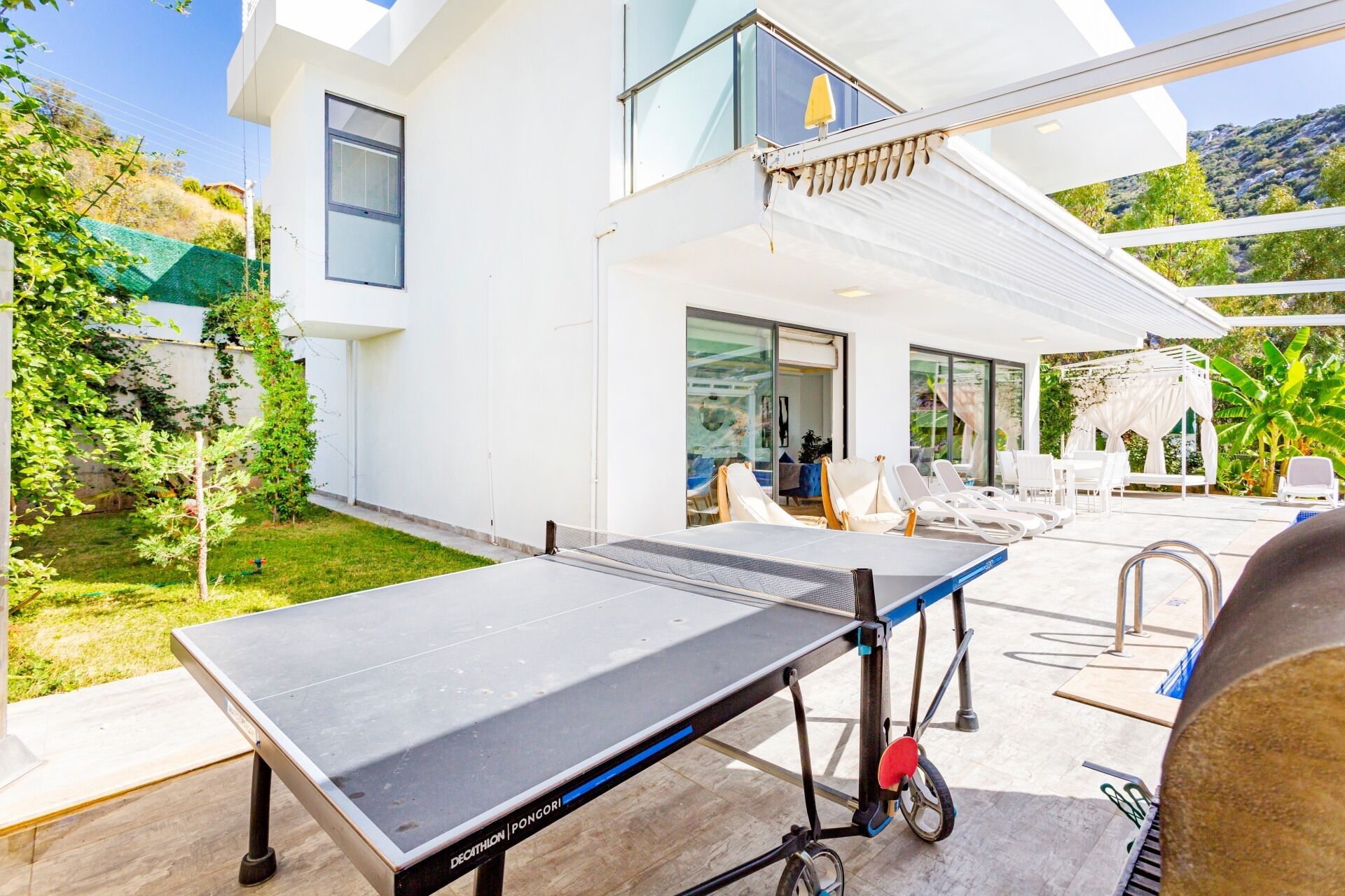 Ein Tischtennistisch steht in einer modernen Außenpatio-Anlage mit Blick auf ein Haus und Grünflächen.