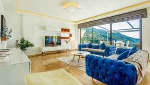 Una sala de estar moderna con un televisor grande, un sofá y un comedor con vistas a las montañas.