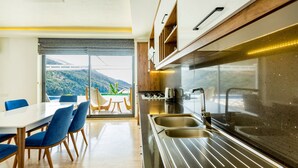 Una cocina moderna con un ventanal grande, un comedor con sillas azules y vistas a un paisaje montañoso.