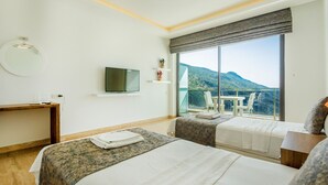 Habitación de hotel con dos camas, televisión, escritorio y balcón con vista a la montaña.