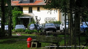 A hotel with a tiled roof, parked cars, and a red trash bin. - Hotel Heidehof (Unna)