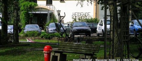 Un hotel con tejado de baldosas, coches aparcados y un contenedor de basura rojo.