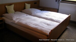 A double bed in a hotel room with two bedside tables, a window with a view of greenery, and a radiator. - Hotel Heidehof (Unna)