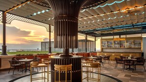 Un salón en la azotea con una chimenea central, asientos al aire libre y una zona de bar.