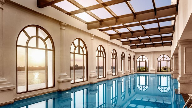 Una piscina interior larga con ventanas arqueadas y vista al agua exterior.