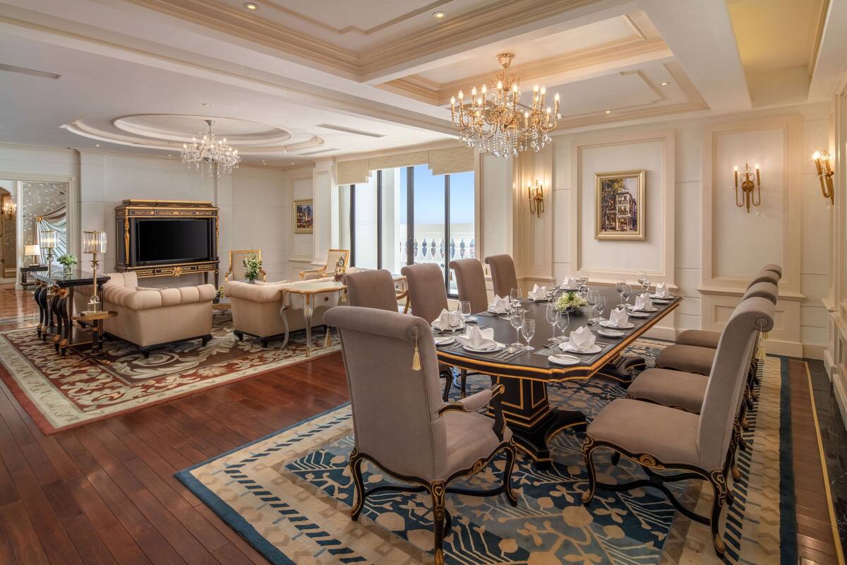 A formal dining room with a large table set for eight, surrounded by upholstered chairs.