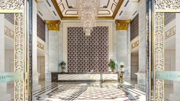 A grand lobby with marble floors, a patterned wall, and a chandelier.