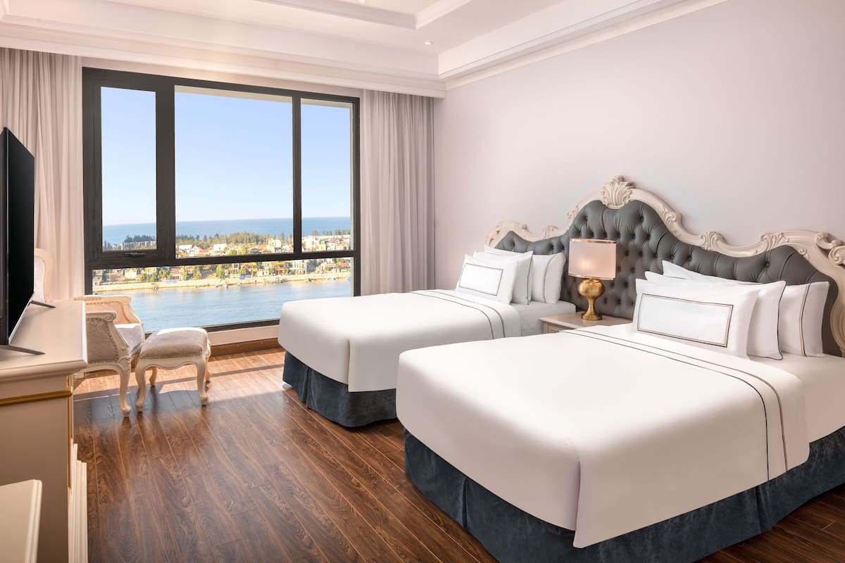 A hotel room with two beds, a desk, and a view of the sea.