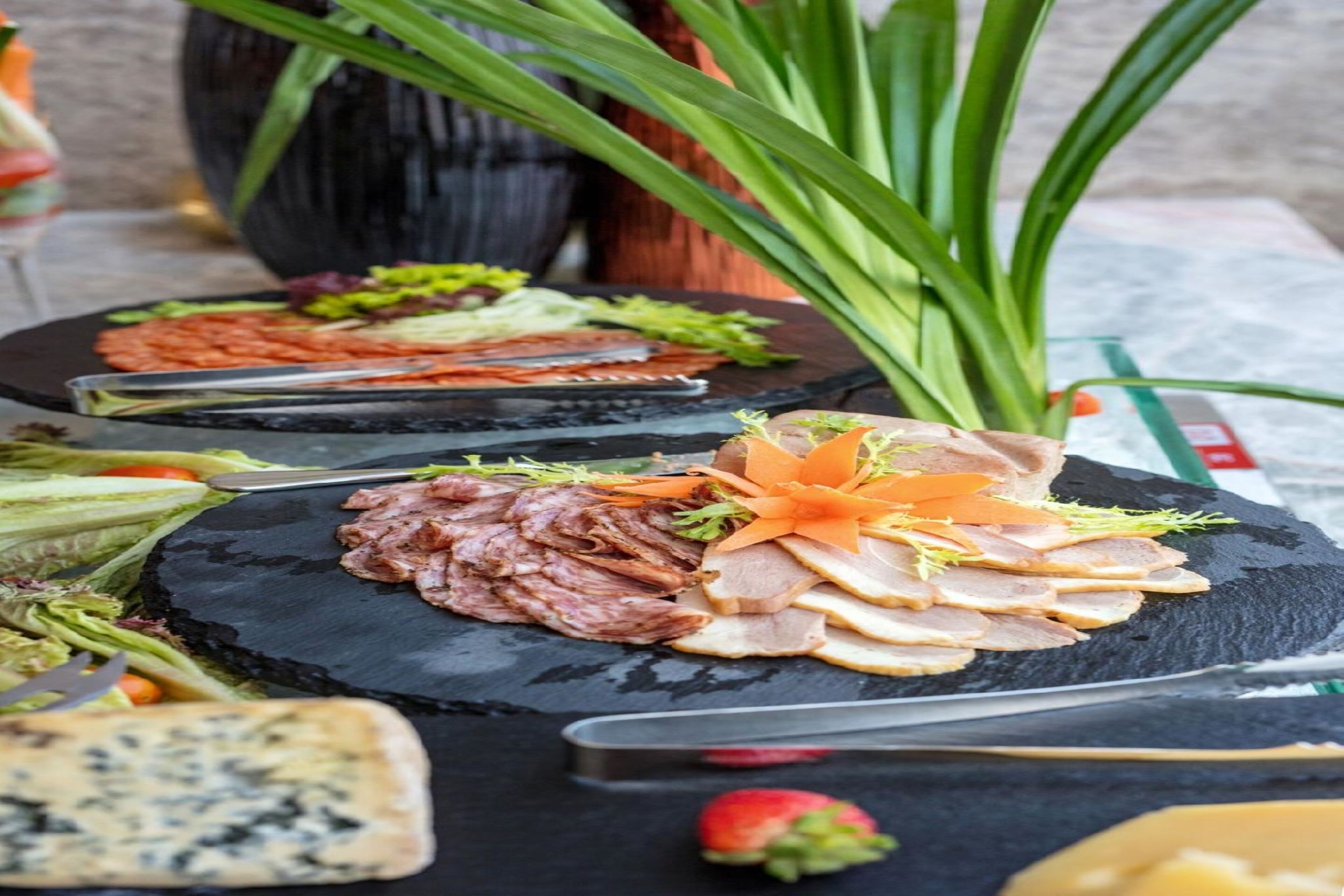 Una tabla de quesos y embutidos con diversas carnes, quesos y adornos sobre una tabla de pizarra.