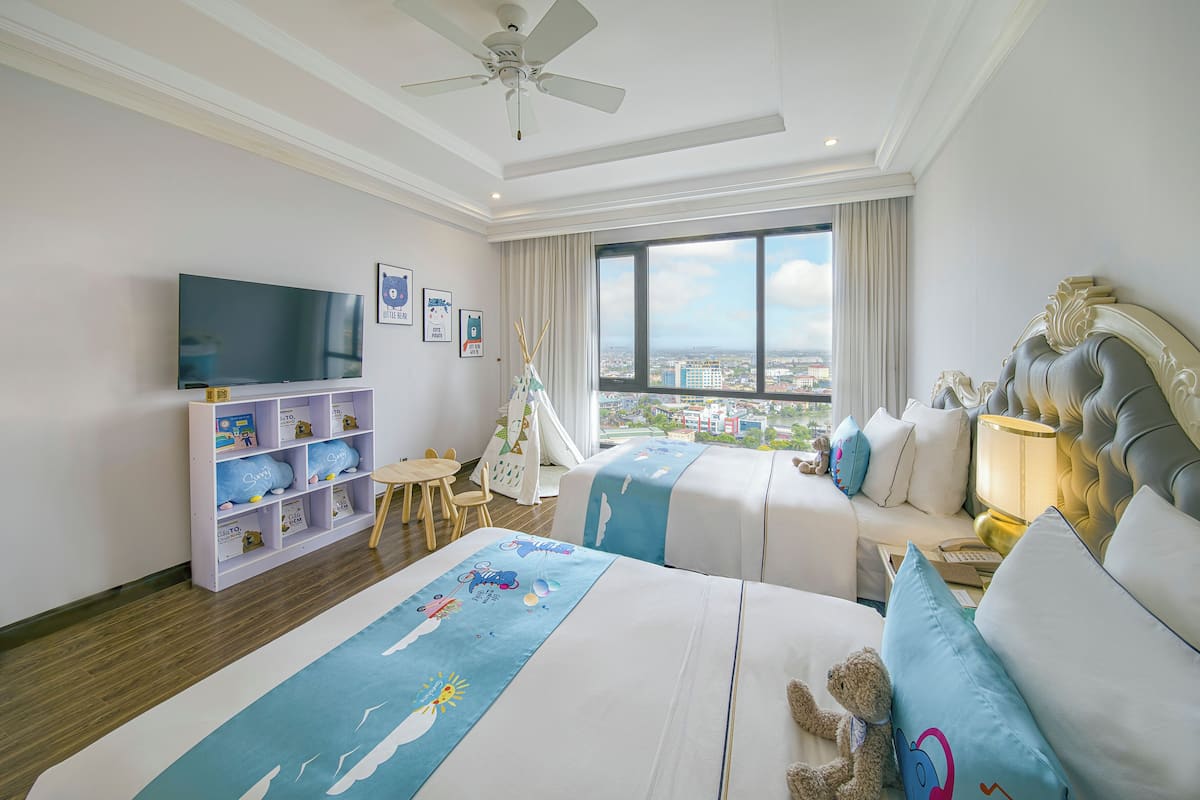 A hotel room with two beds, a TV, a bookshelf, and a view of the city.