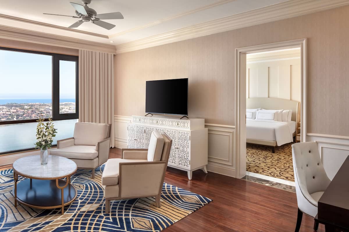 A hotel room with a large window, a flat-screen TV, a white cabinet, a bed, and a round coffee table.