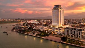 Un hotel de gran altura con un letrero llamativo, ubicado junto a un muelle con barcos y un paisaje urbano al fondo.