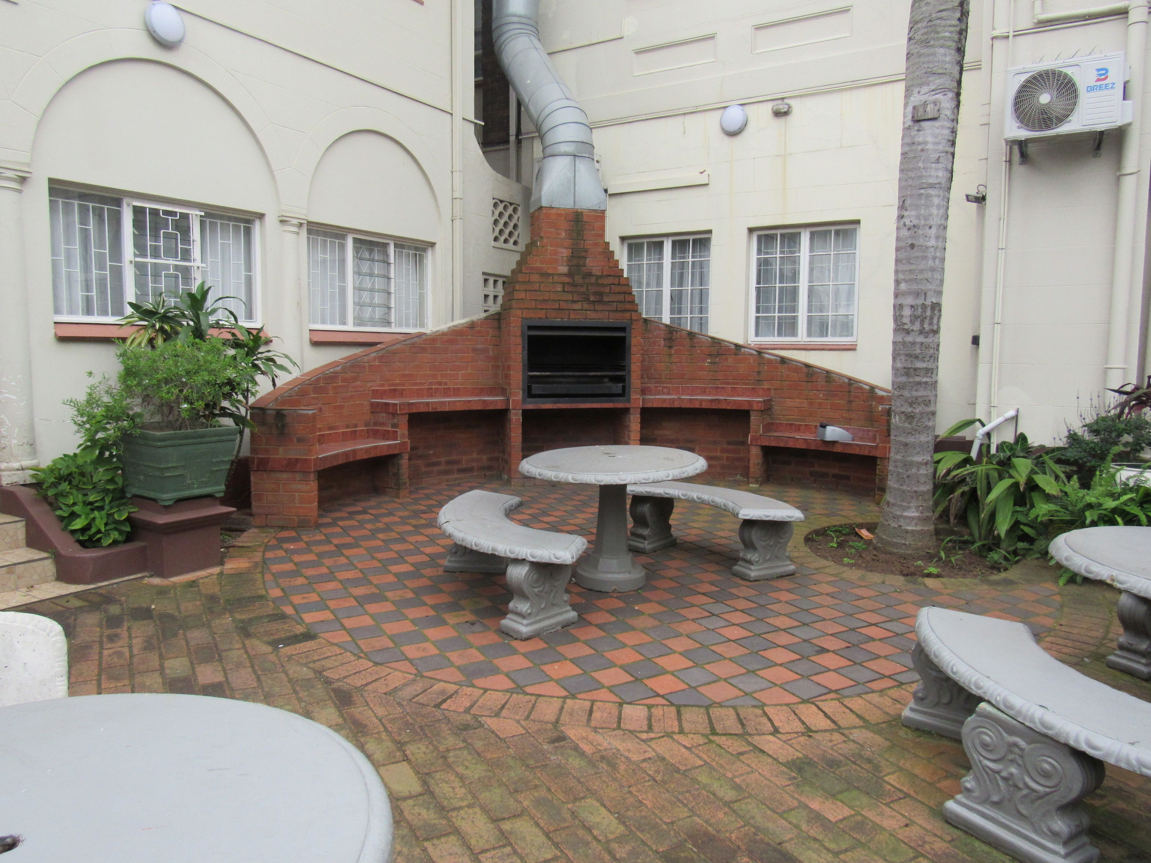 Un espace extérieur aménagé en terrasse, avec une cheminée en briques, des tables en pierre et des plantes en pot.