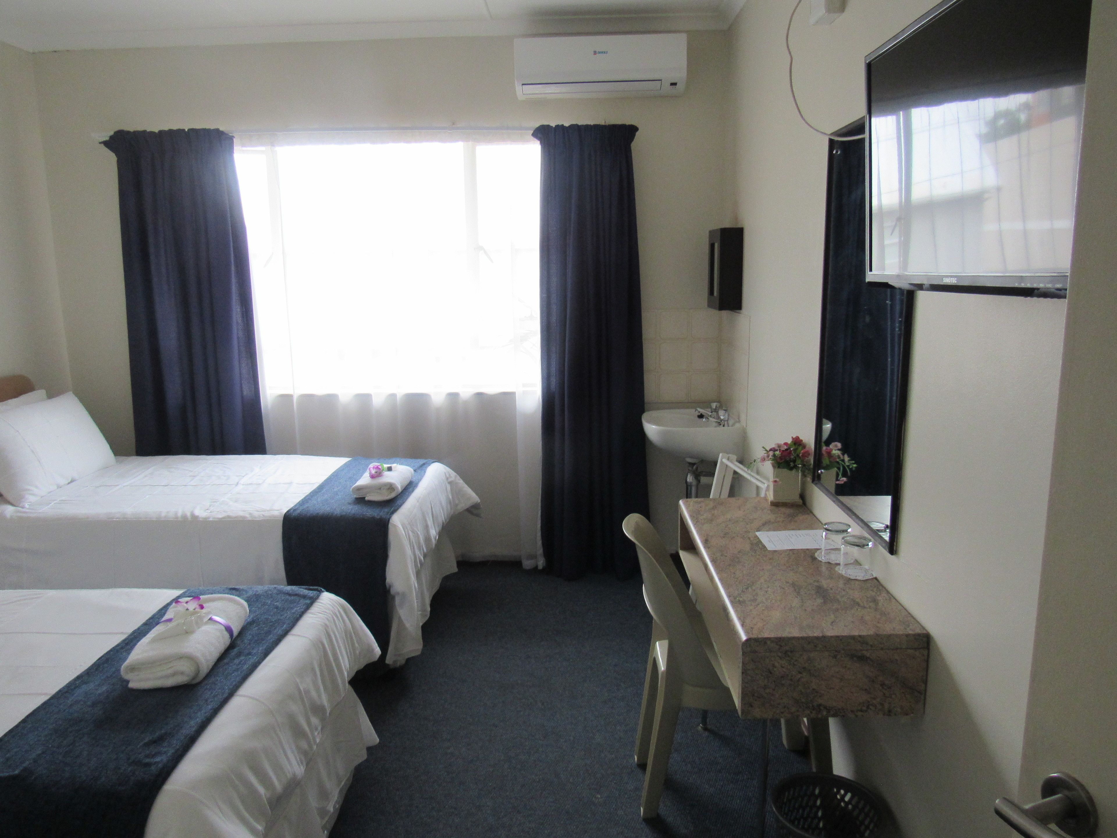 A hotel room with two beds, a desk, a chair, a sink, and a mirror.