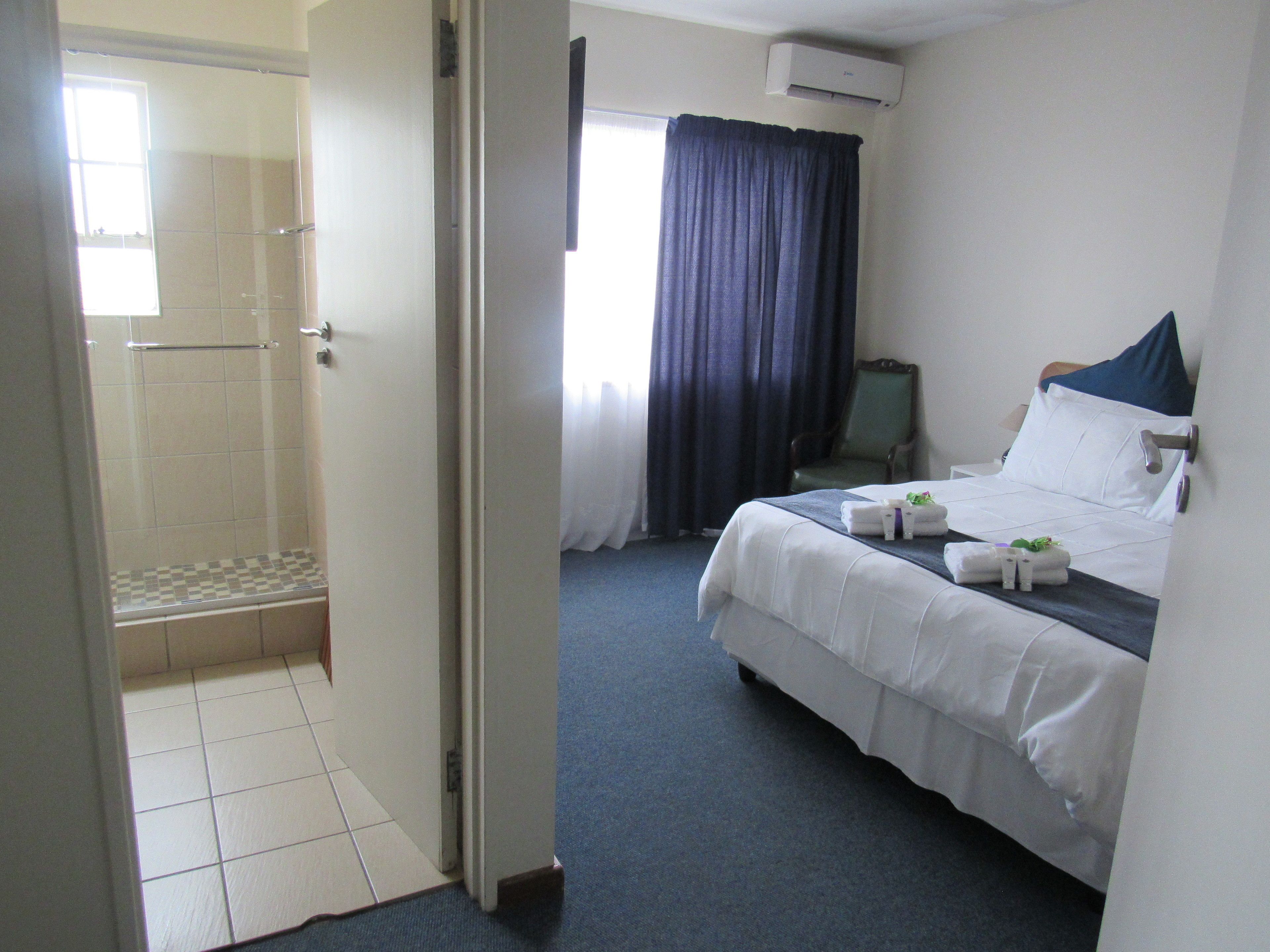 A hotel room with a shower, a bed with white linens, a chair, and a window with curtains.