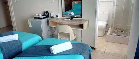 Habitación de hotel con dos camas, un escritorio, un espejo, un televisor, ducha y un refrigerador pequeño.