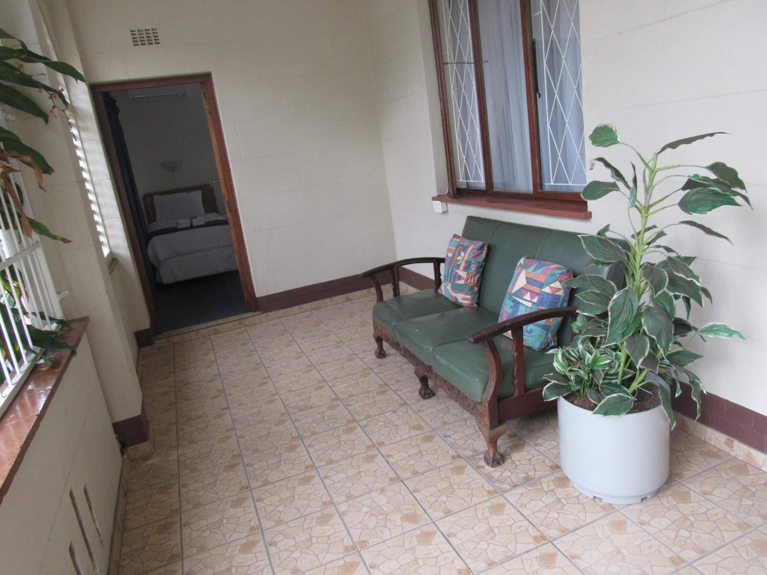A hallway with a green sofa, a potted plant, and a window with curtains.