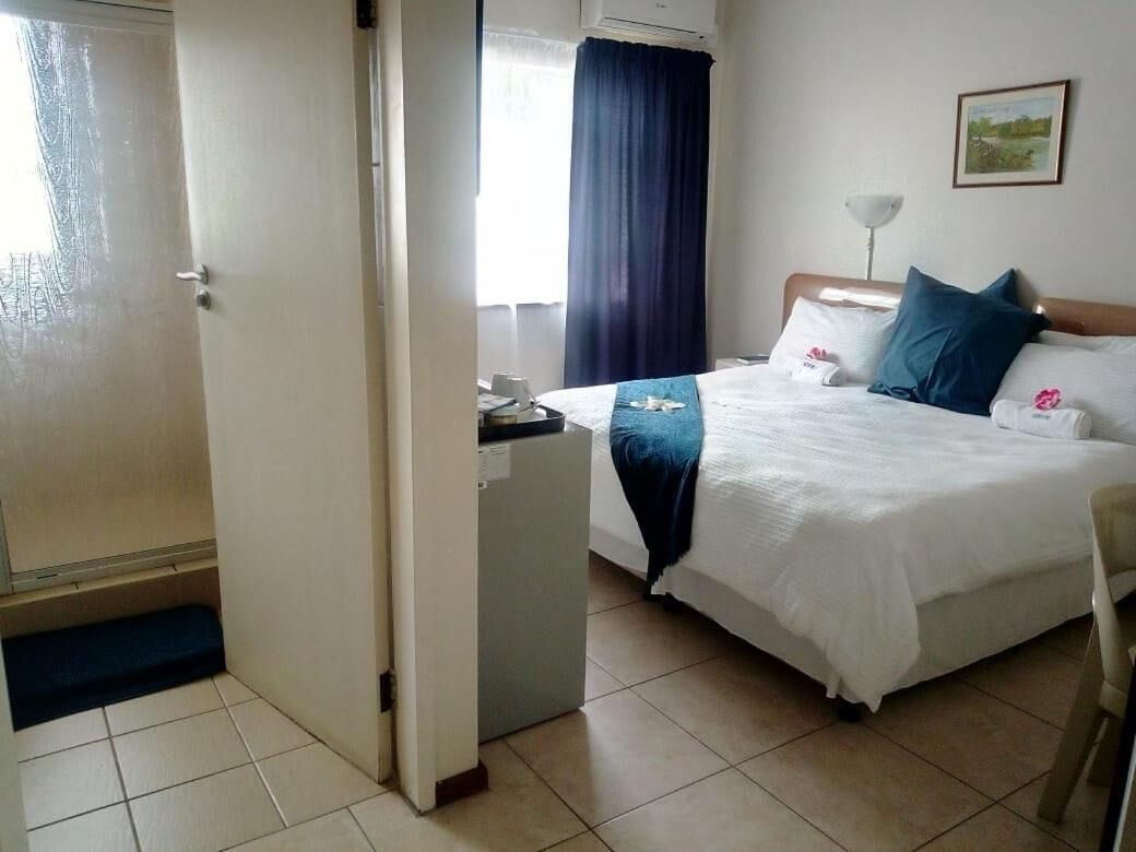A hotel room with a bed, a desk, a chair, a lamp, and a painting on the wall.