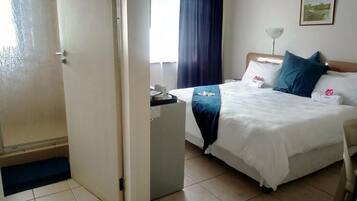 A hotel room with a bed, a desk, a chair, a lamp, and a painting on the wall.
