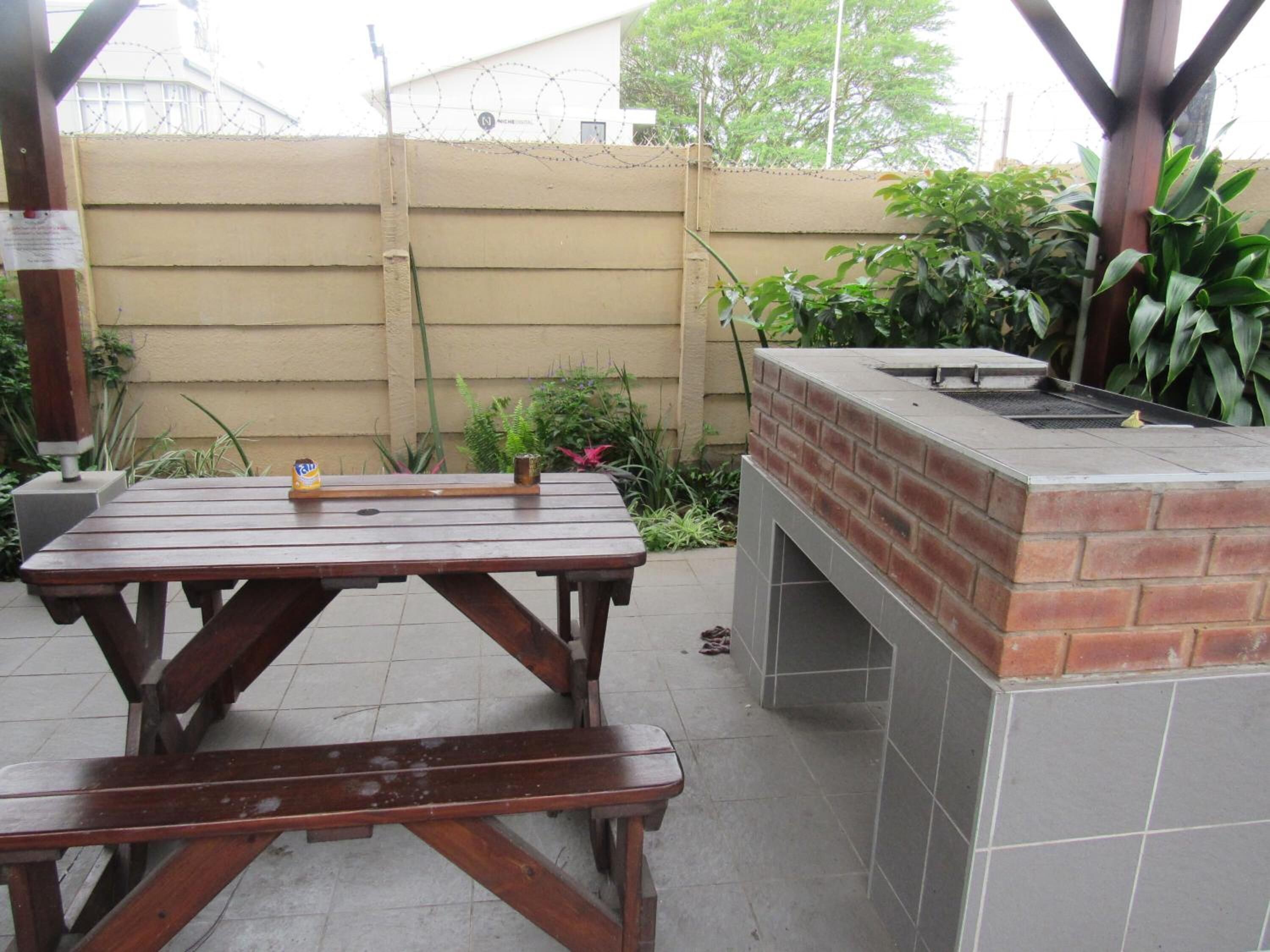 An outdoor patio with a brick barbecue grill and a wooden picnic table.