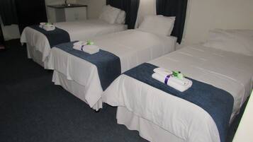 A hotel room with two single beds, each with a neatly folded towel and a small flower. There is a bedside table with a lamp and a mirror.