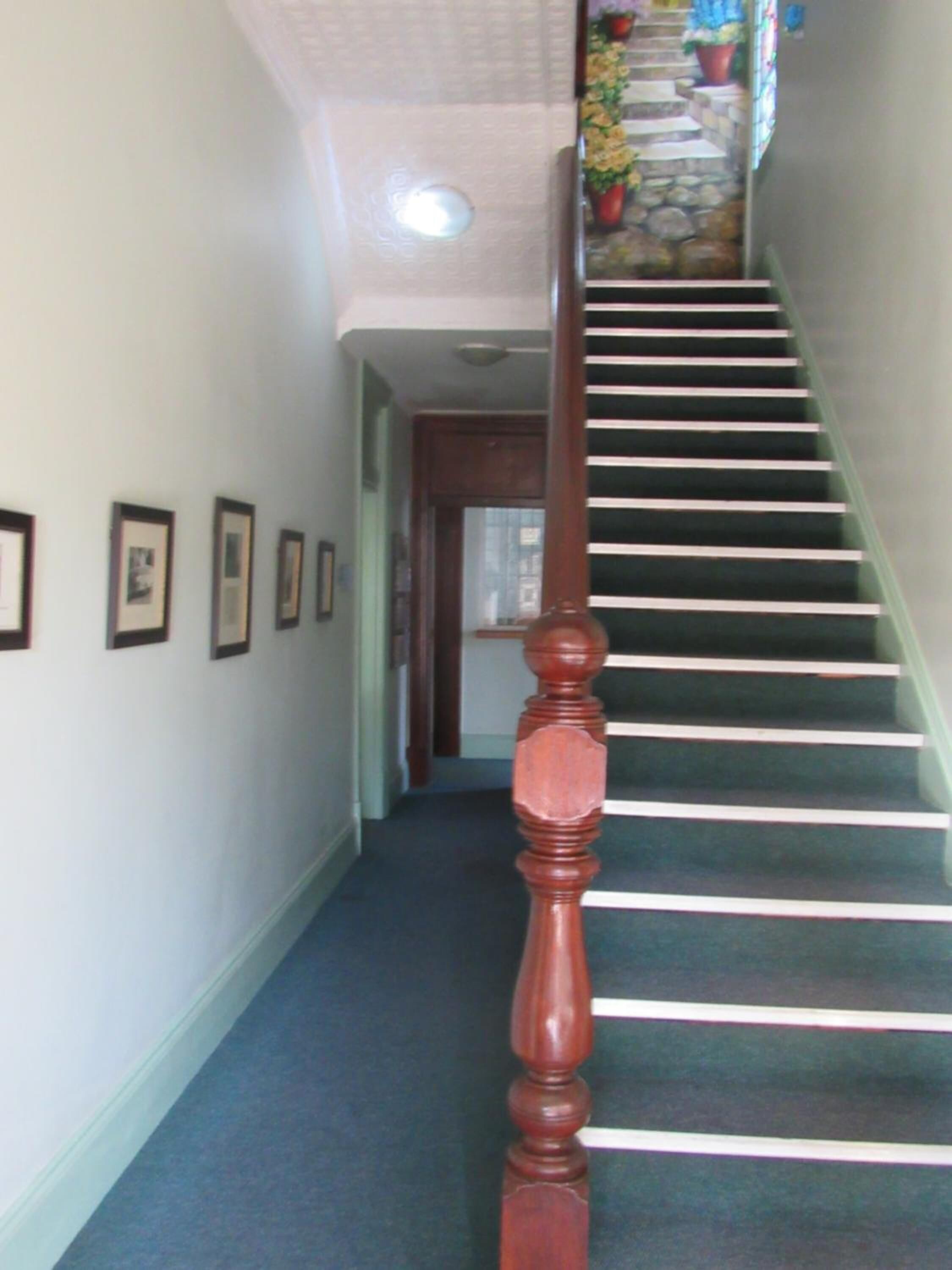Una escalera con balaustres de madera y piso alfombrado que conduce a una plataforma.