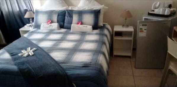 A hotel room with a bed, two bedside tables, a lamp, a refrigerator, and a window with curtains.