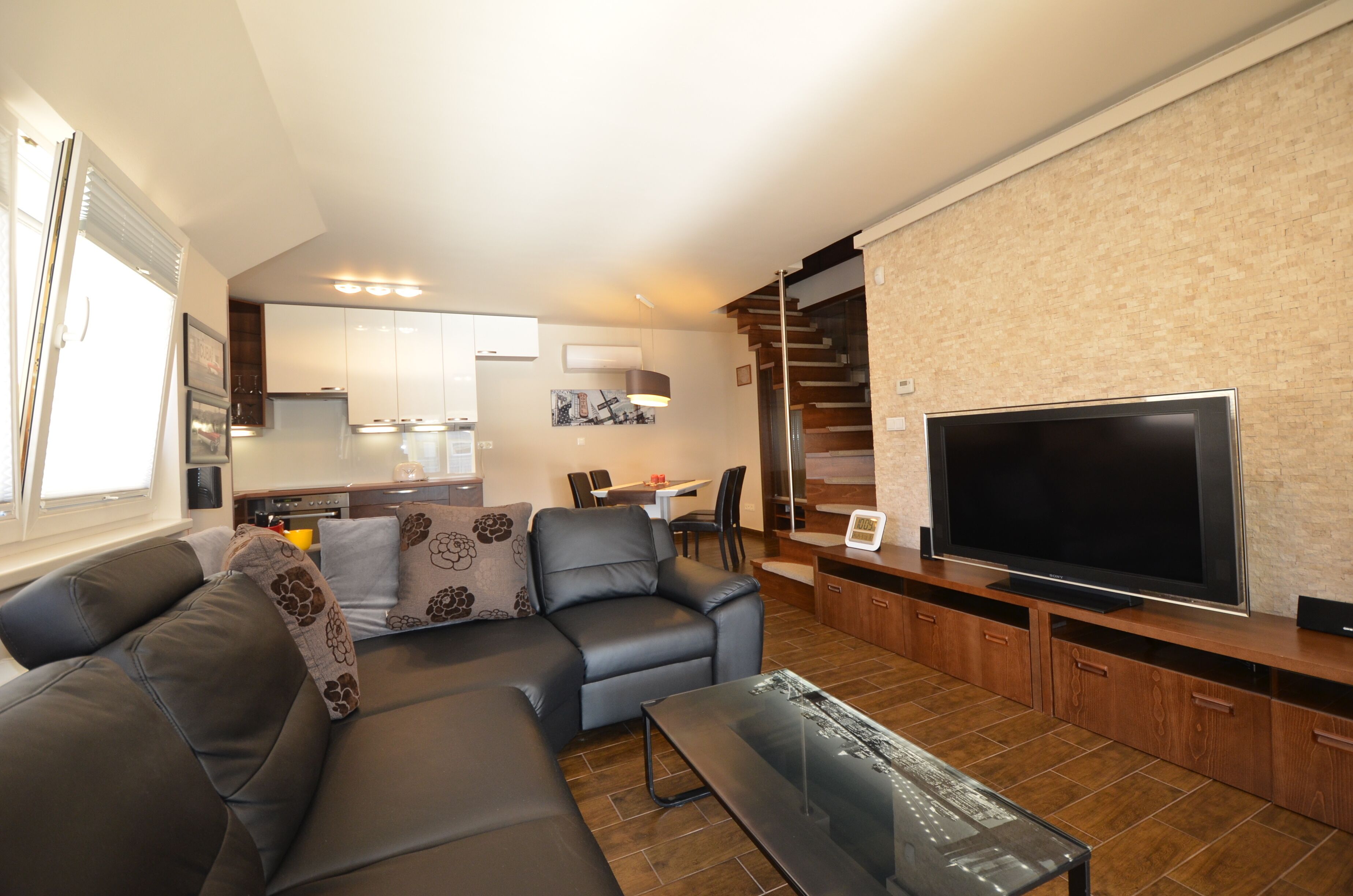 A modern living room with a sectional sofa, a flat-screen TV, and a dining area with a table and chairs.