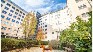 Une aire de jeux avec une balançoire et un banc, entourée d’immeubles et d’arbres.