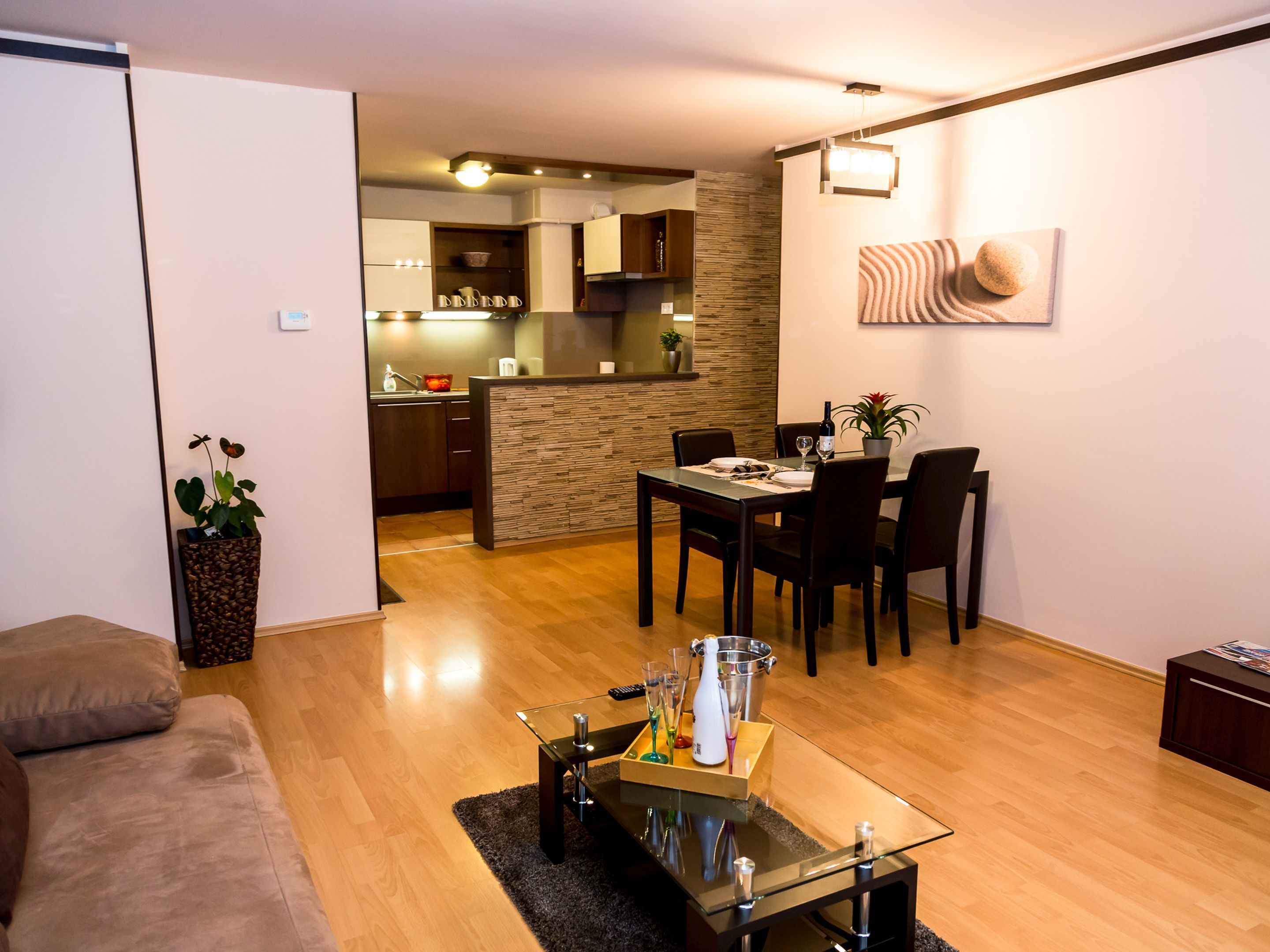 A modern living room with a glass coffee table, a dining area with a table and chairs, and a kitchen in the background.