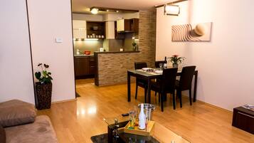 A modern living room with a glass coffee table, a dining area with a table and chairs, and a kitchen in the background.