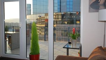 A modern living room with a glass door leading to a balcony, a potted plant, a small table, and a couch.