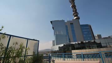 Un edificio moderno con una estructura de torre distintiva, rodeado de plantas en macetas y una barandilla azul.