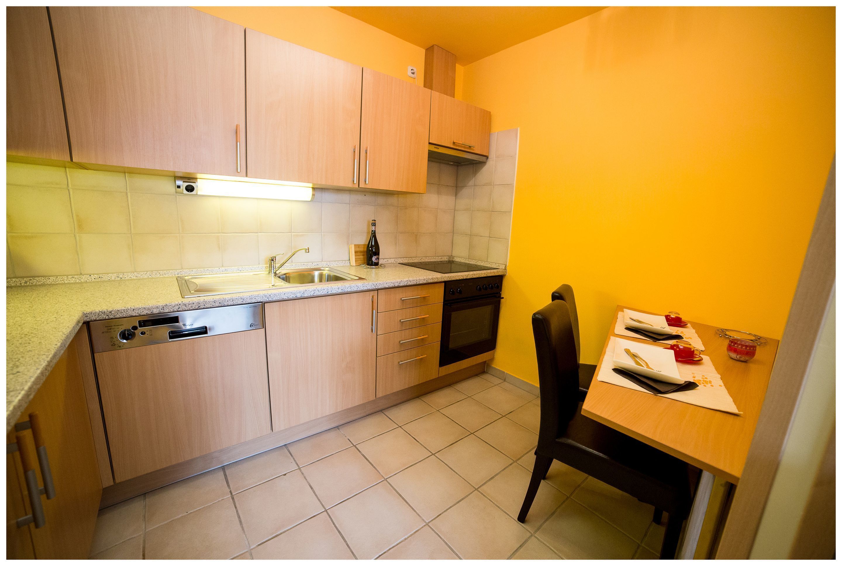 Una cocina compacta con armarios de madera, lavavajillas, horno y mesa con sillas.