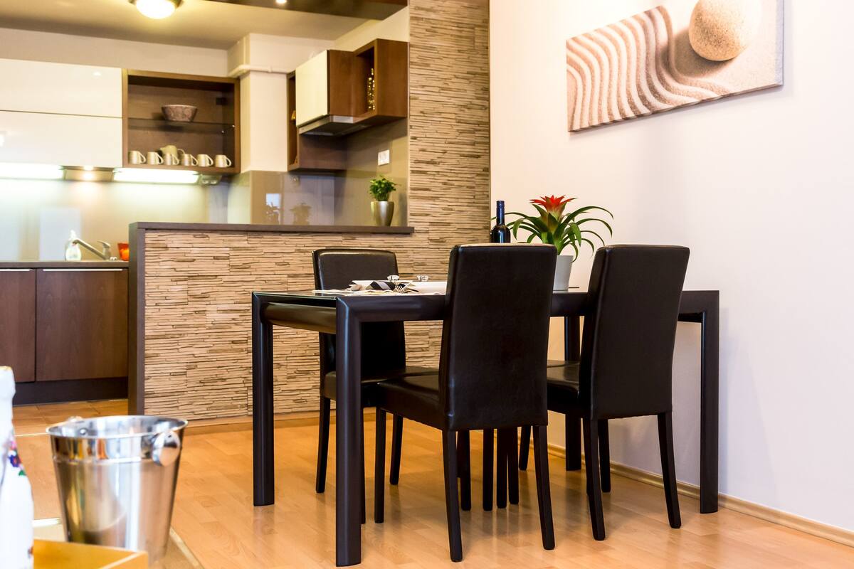 A modern dining area with a black table and chairs, a small potted plant, and a decorative wall piece.