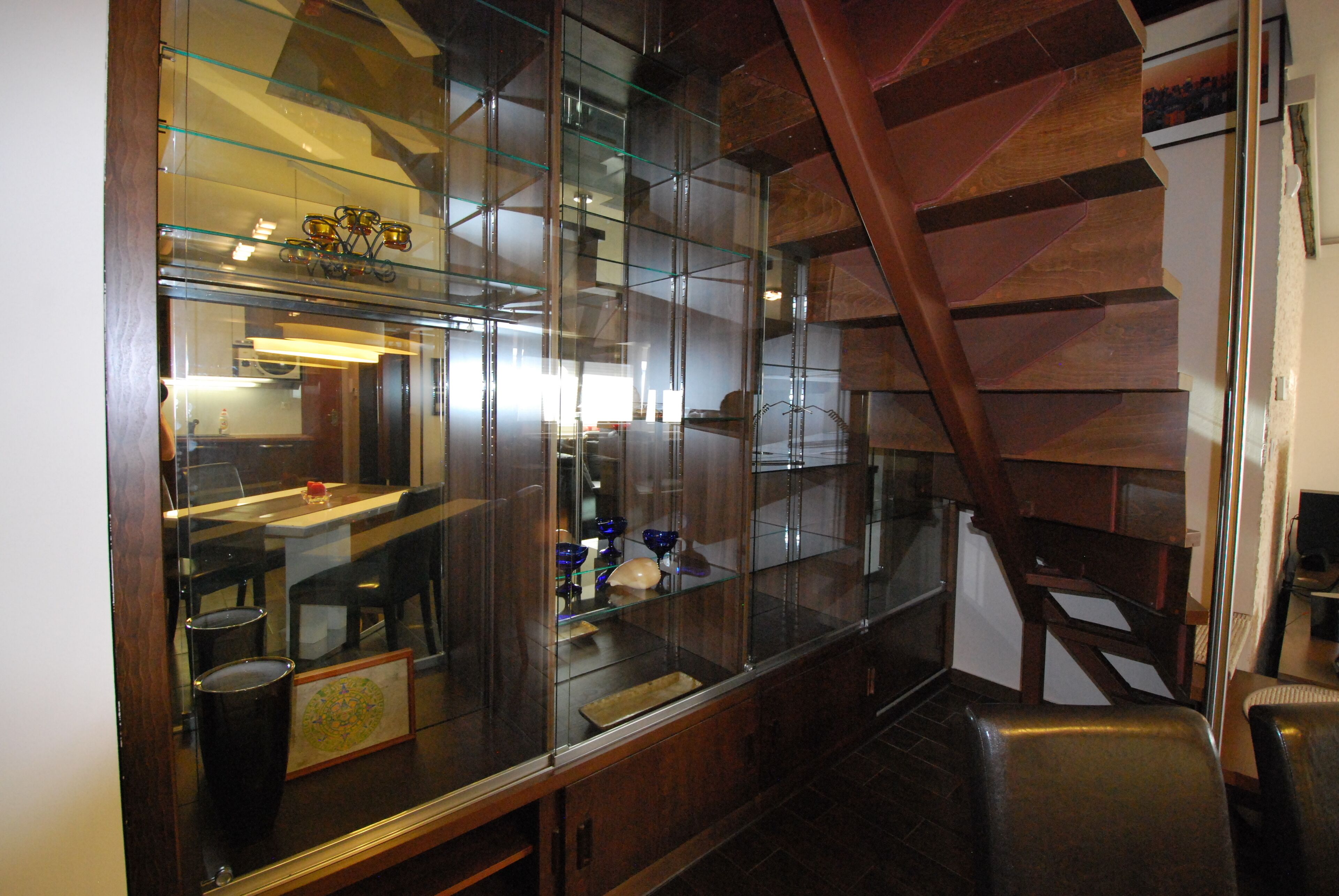 Una cocina moderna con armarios de vidrio, una escalera de madera y un comedor con sillas y una mesa.