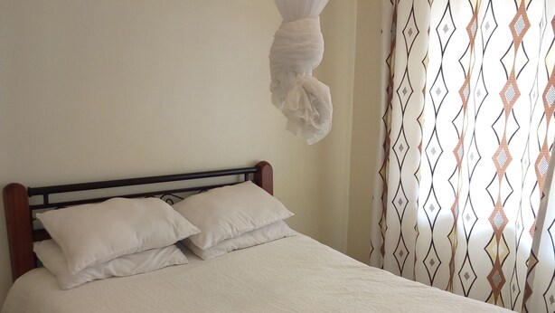 A neatly made bed with white linens and a canopy, a wooden headboard, and a patterned curtain. - Kadana Bed & Breakfast - Adults Only (Nairobi)