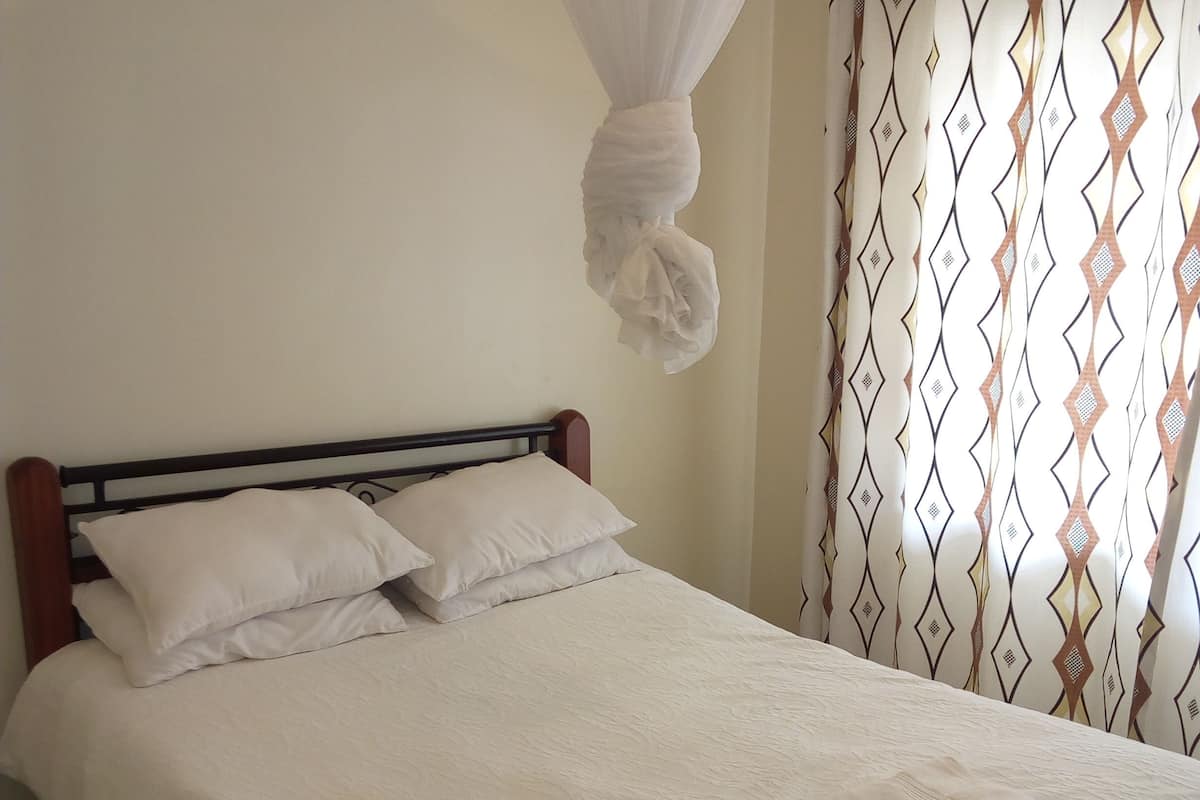 Un letto rifatto con lenzuola bianche e un baldacchino, una testiera in legno e una tenda fantasia.