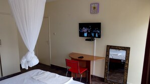 A hotel room with a bed, a desk, a chair, a television, and a mirror. - Kadana Bed & Breakfast - Adults Only (Nairobi)