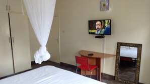 A hotel room with a bed, a desk with a chair, a television, and a mirror. - Kadana Bed & Breakfast - Adults Only (Nairobi)