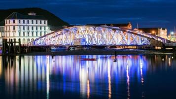 A large, illuminated bridge with a symmetrical truss design, spanning over a body of water with a calm reflection.