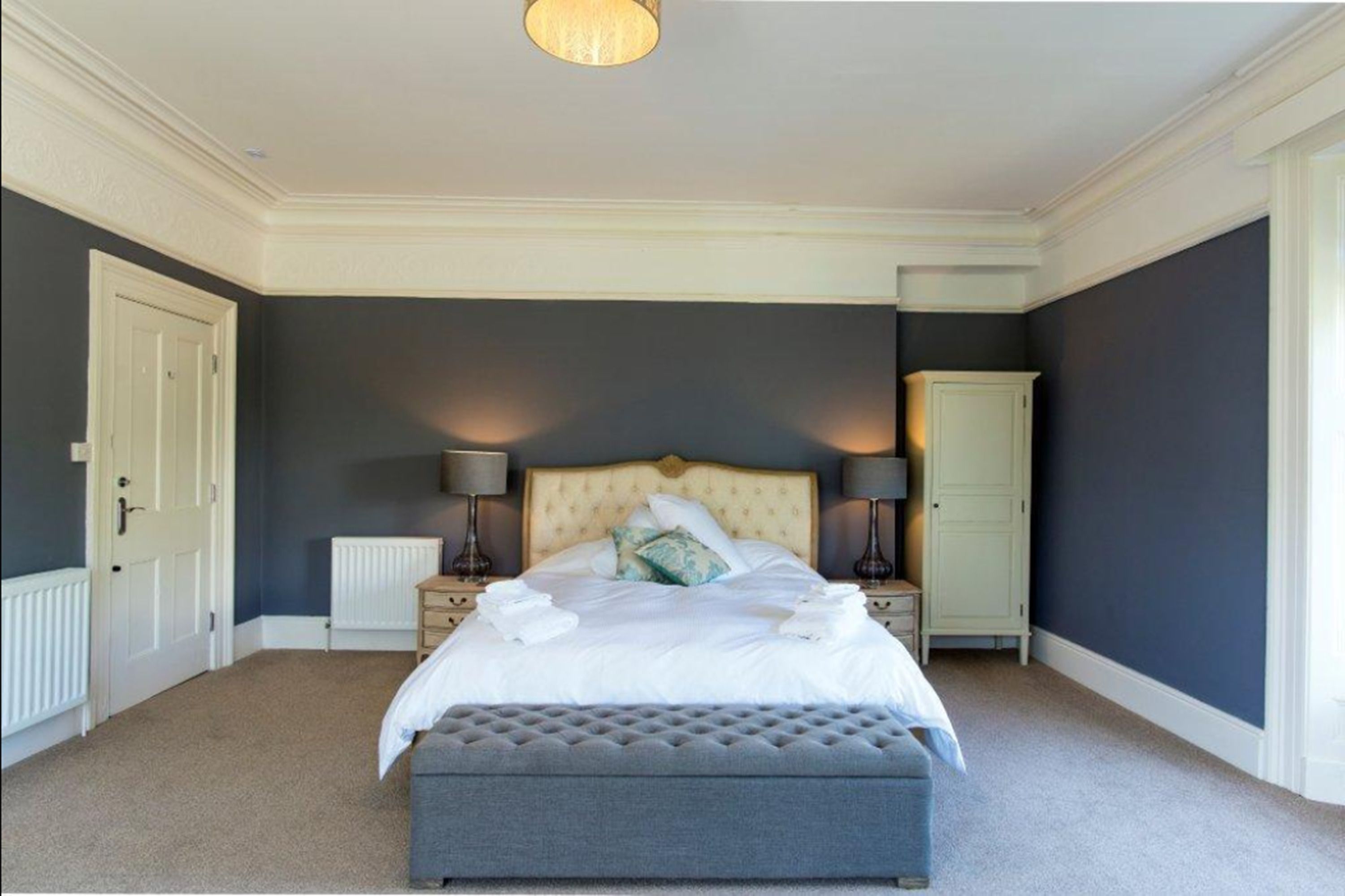 Een slaapkamer met een groot bed, twee bedlampen, een dressoir en een radiator.