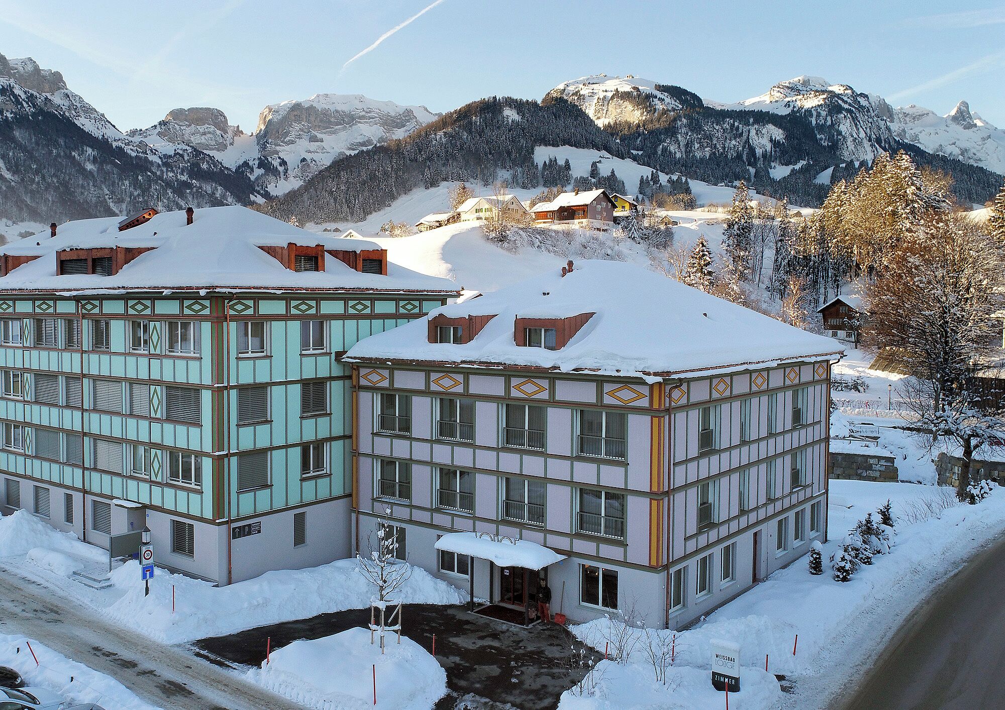 A hotel with traditional architecture, a snow-covered landscape, and mountains in the background.
