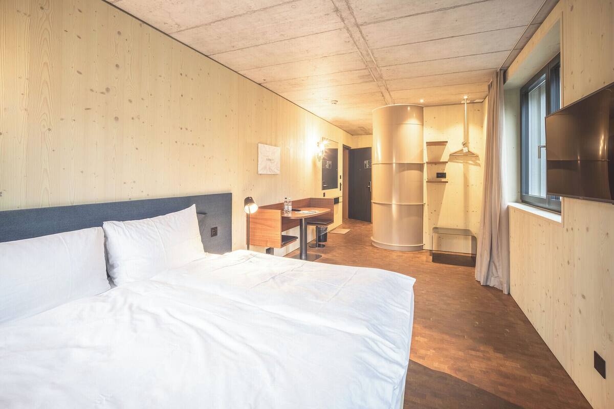 A hotel room with a large bed, wooden walls, a desk with a chair, a mirror, and a TV mounted on the wall.