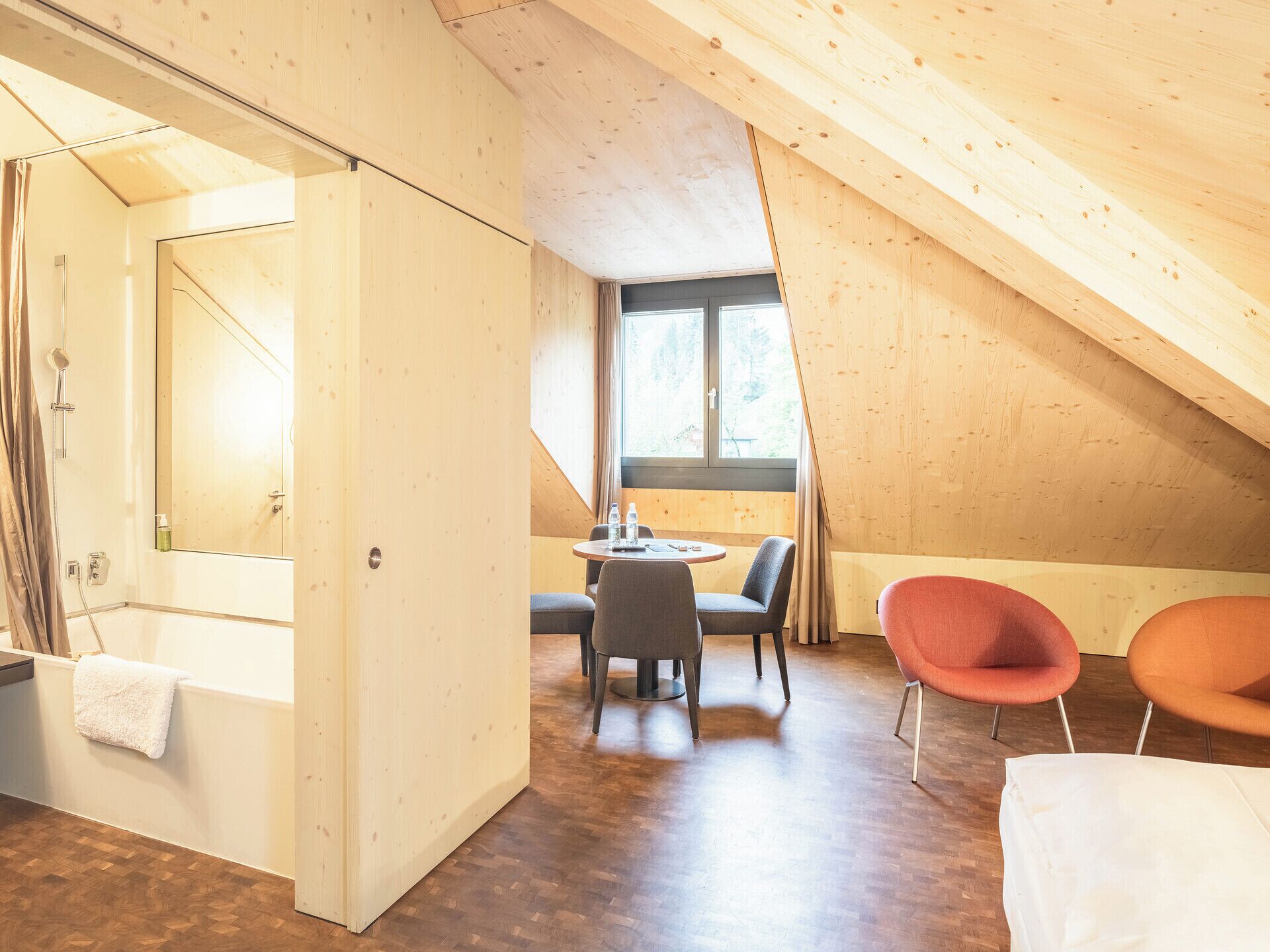 A modern, wooden interior with a small dining area, two chairs, and a view through a window.