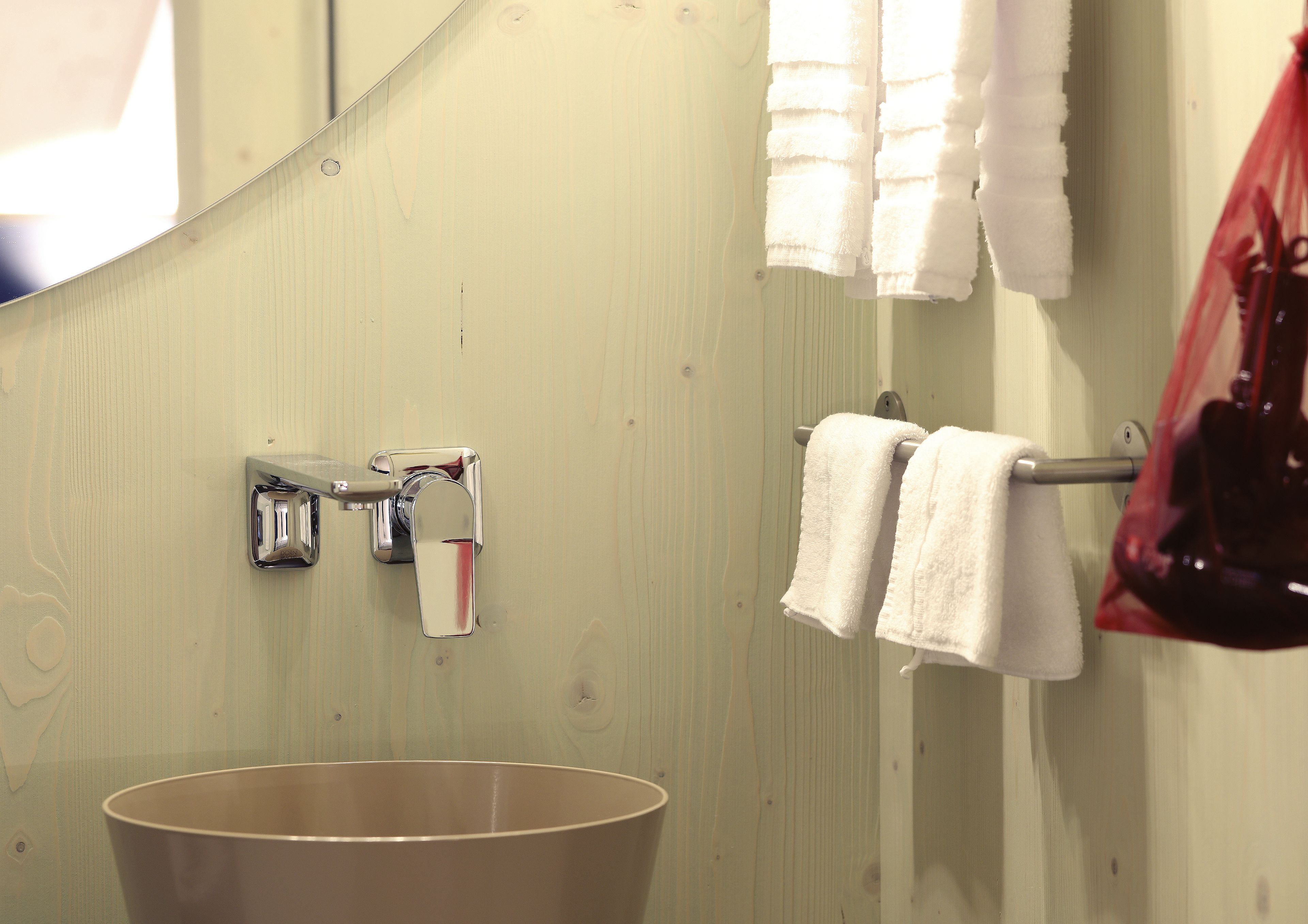 Une salle de bain avec un lavabo, un porte-serviettes avec deux serviettes blanches, un sac rouge et un miroir.