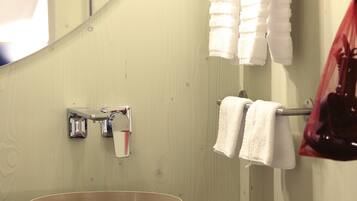 Une salle de bain avec un lavabo, un porte-serviettes avec deux serviettes blanches, un sac rouge et un miroir.