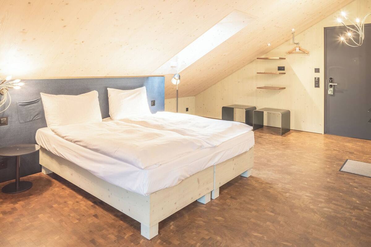 A modern bedroom with a sloped ceiling, a bed with white linens, a bedside table, and a wall-mounted light fixture.